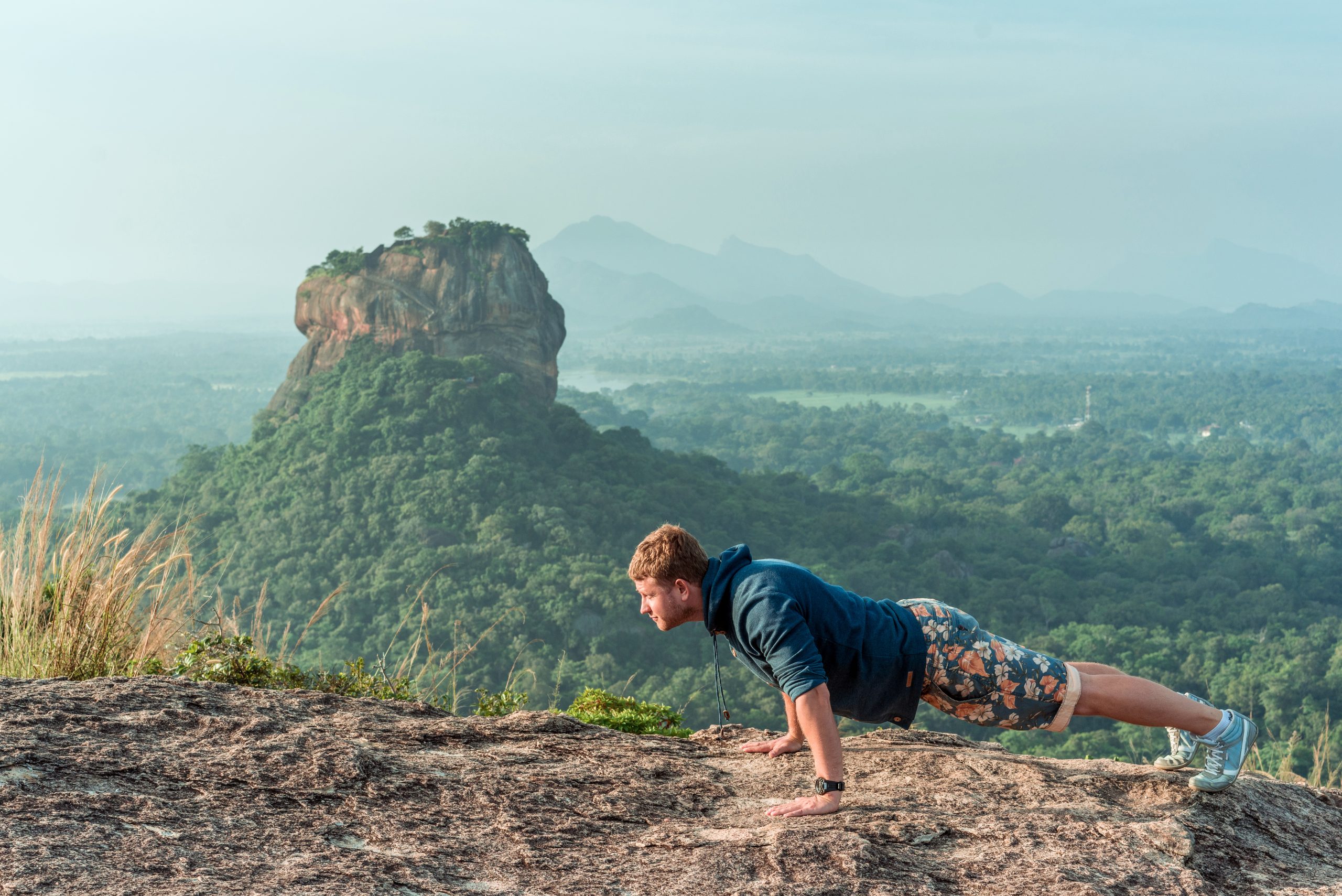 Concentrated strong young man doing push-ups on the floor with the mountains on a sunny warm day. Healthy lifestyle and fitness concept